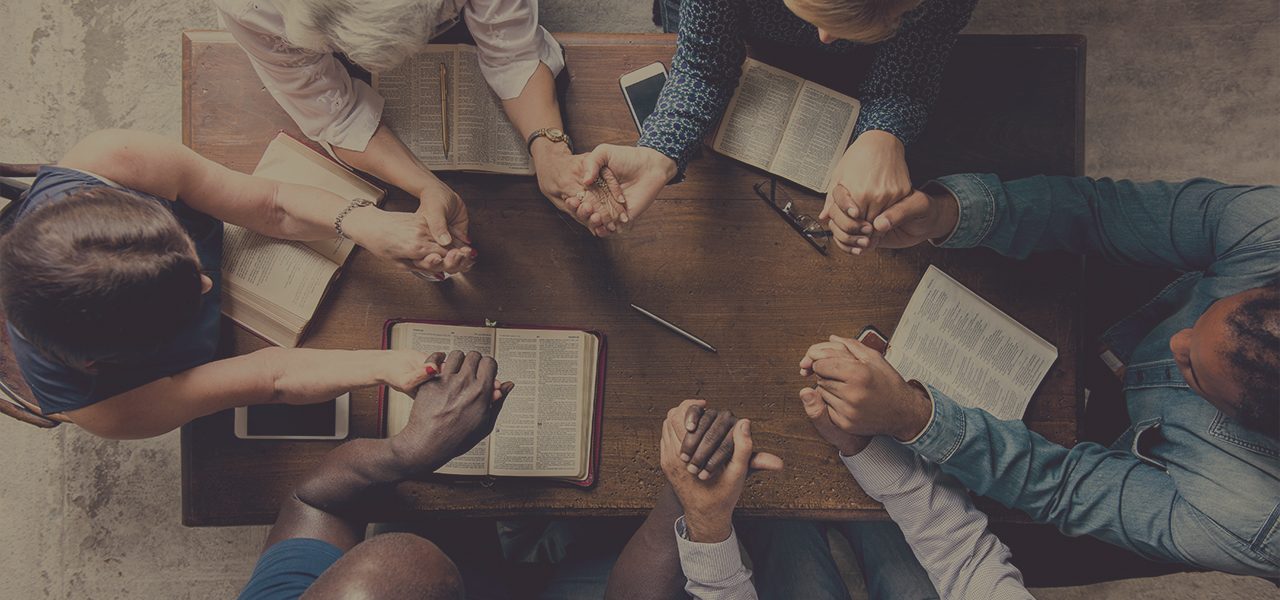 group of people holding hands around a wooden table